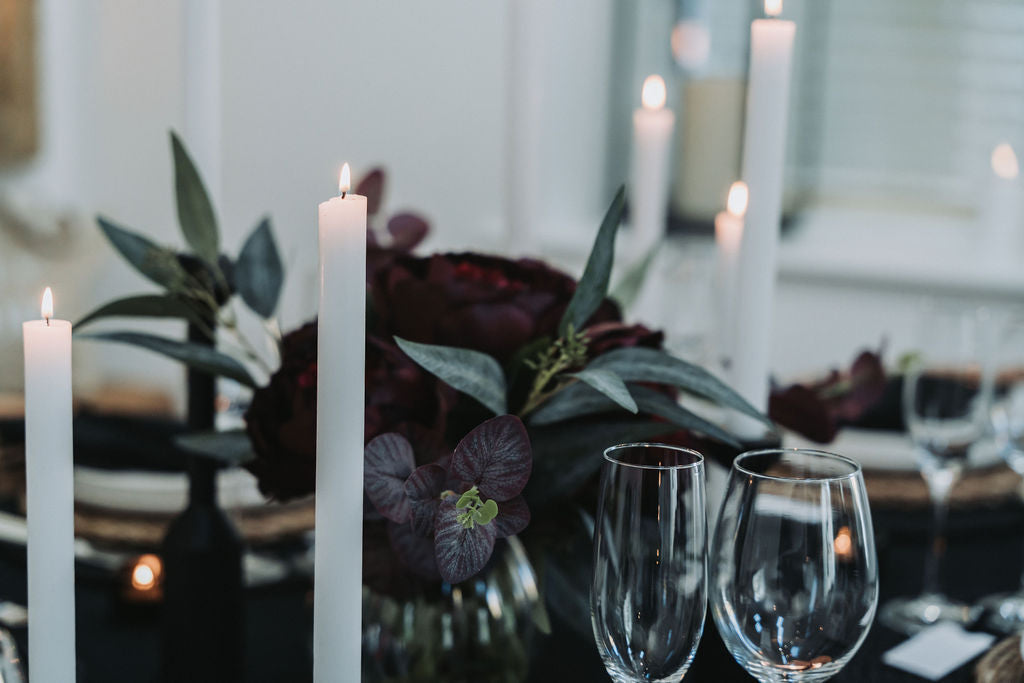 Decorative table setting with white taper candles, flowers, and wine glasses by Noble & Nordic.