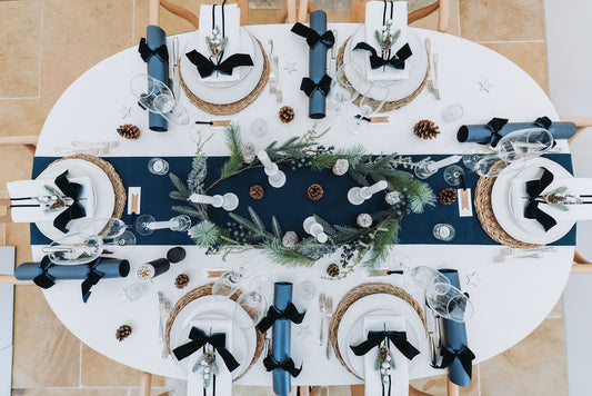 Decorative navy Christmas table setting with a blue runner, fire pine garland, and navy crackers with navy velvet bow designed by Noble & Nordic.