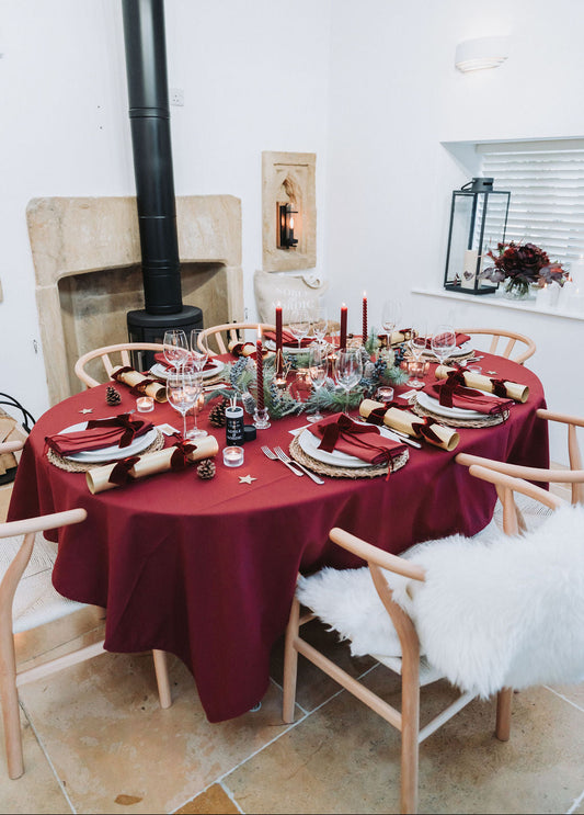 Burgundy Christmas Dining table set for a festive meal with dark red tablecloth, burgundy candles, and decorative items in a nordic country styled room, designed by Noble & Nordic.