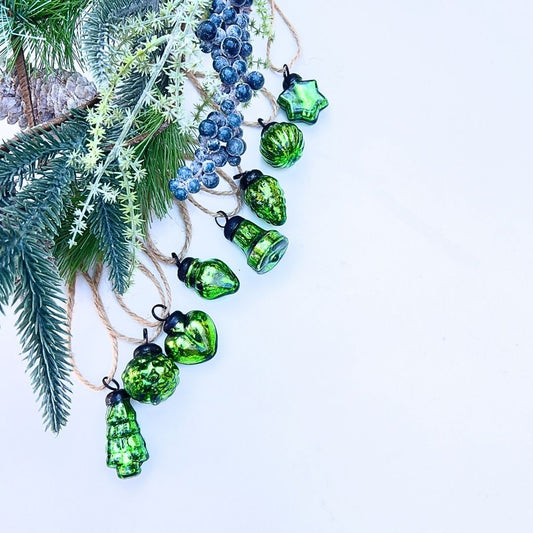 Green glass Christmas baubles on a white background with pine branches.