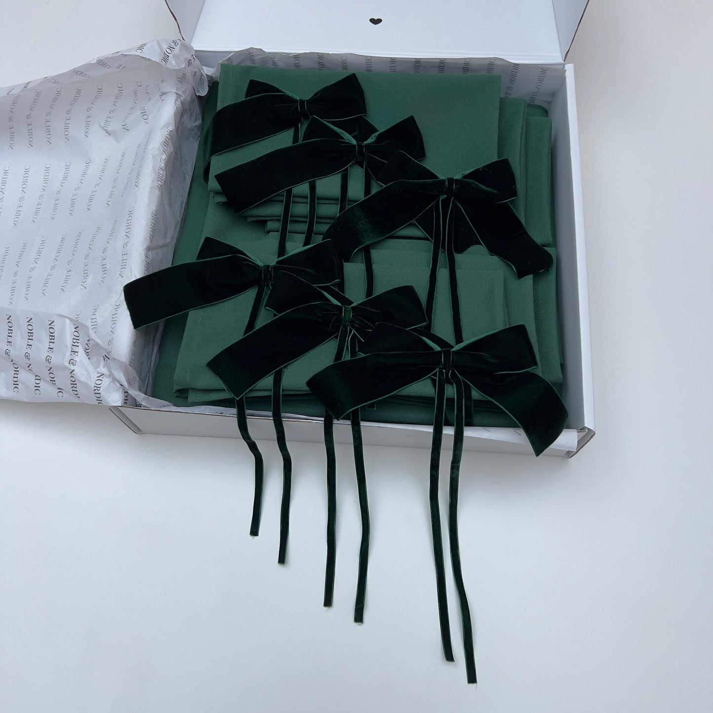 Dark Green Velvet bows on green table linen inside an open box with white interior.