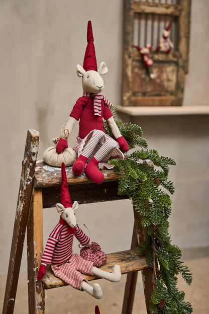 Two handmade fabric reindeer dolls dressed in red and white striped outfits and pointed red hats, posed on a rustic wooden ladder with a green pine garland draped over it.