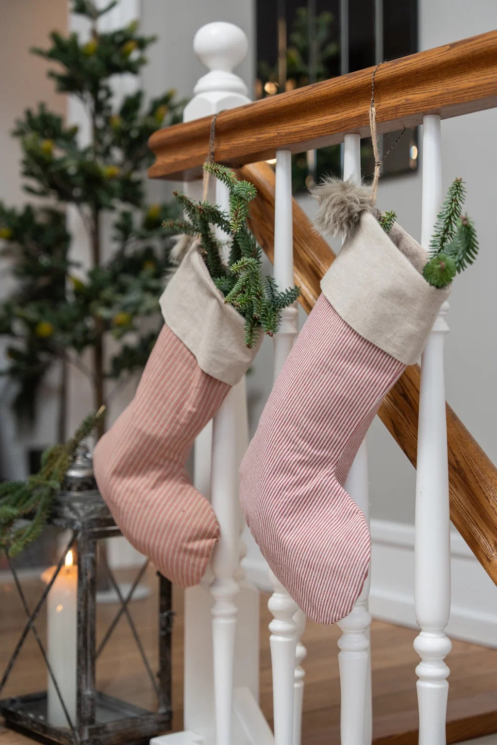 Two Christmas stockings hanging from a wooden banister. One stocking is dusty pink corduroy with a cream fabric cuff and a green pine sprig tucked inside.