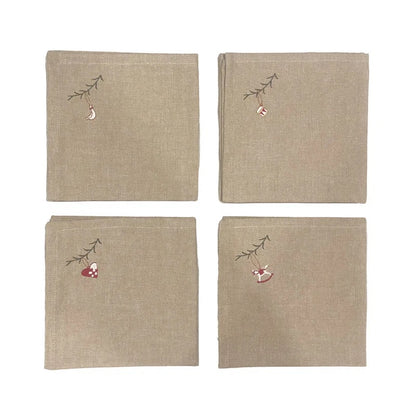 Four beige linen napkins arranged in a 2x2 grid on a white background. Each napkin features a small embroidered Christmas motif in the top-left corner, including a hanging ornament and a red-and-white stocking on a small branch.