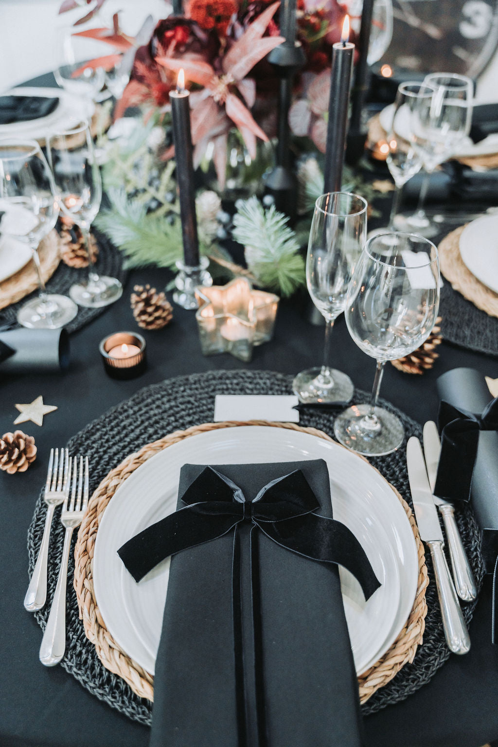 Elegant table setting with black napkin, white plates, and silverware on a black tablecloth by Noble & Nordic.