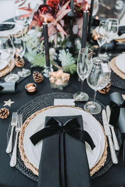 Elegant table setting with black napkin, white plates, and silverware on a black tablecloth by Noble & Nordic.