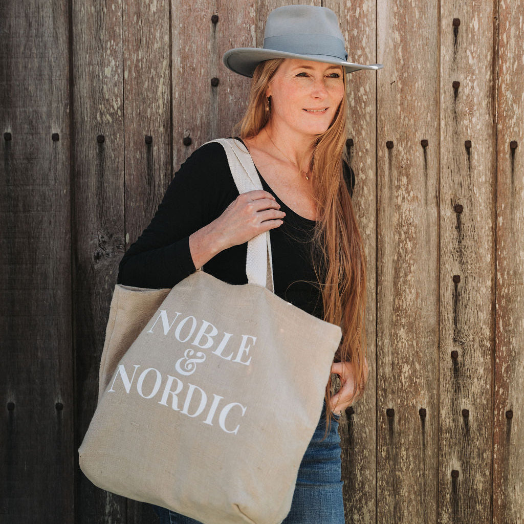 Noble & Nordic founder Inge Nielsen  holding a 'Noble & Nordic' tote bag against a vintage wooden wall