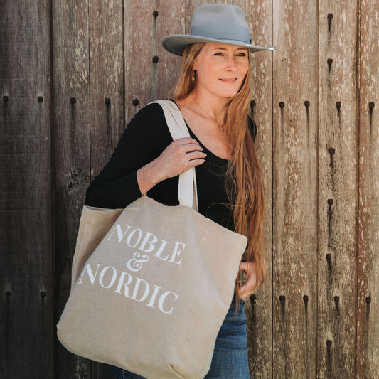 Noble & Nordic founder Inge Nielsen  holding a 'Noble & Nordic' tote bag against a vintage wooden wall