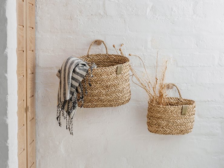 Two woven natural-fiber baskets hanging on a white brick wall, with a striped throw draped over the larger basket and dried stems in the smaller one.