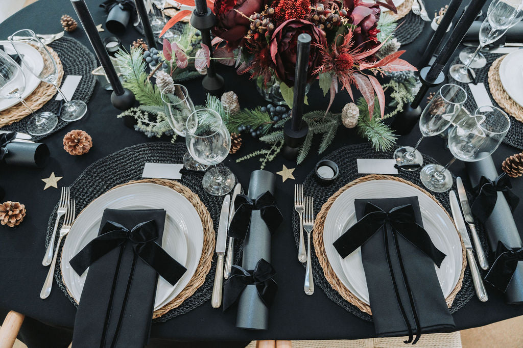 Elegant table setting with black napkins, silverware, and decorative elements on a black tablecloth by Noble & Nordic.