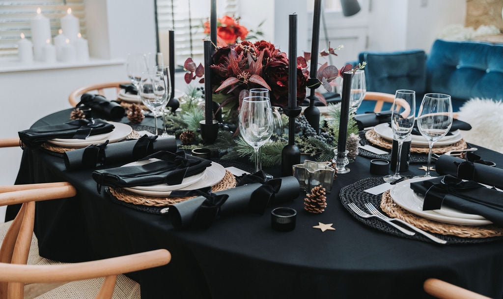 Elegant table setting with black tablecloth, black napkins, and decorative christmas floral centrepieces by Noble & Nordic.
