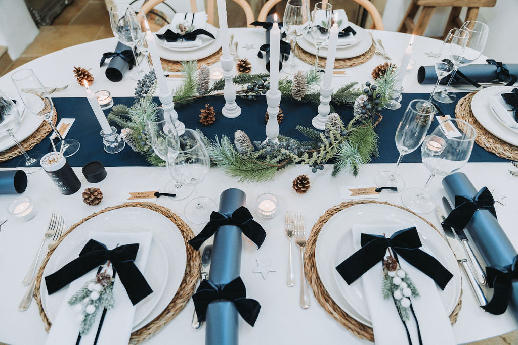 Elegant navy christmas table setting with navy velvet bows, white plates, seaweed placemats and unique Christmas decorative centrepiece, designed by Noble & Nordic.