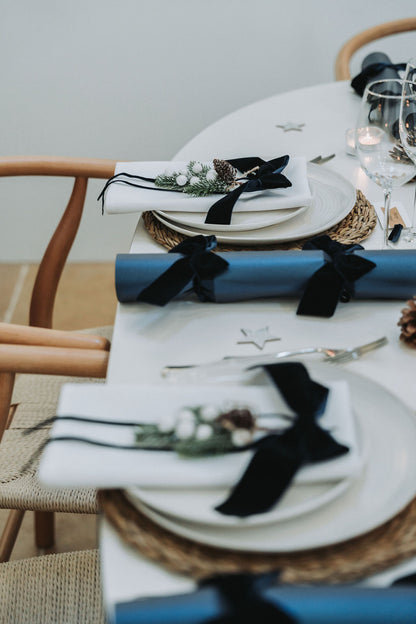 Decorative table setting with navy velvet bows and white plates with navy blue Christmas crackers with navy velvet bows, designed by noble & Nordic
