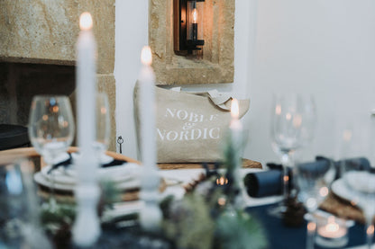 Dining table setting with white candles and a 'Noble & Nordic' branded jute bag in the background, designed by Noble & Nordic.