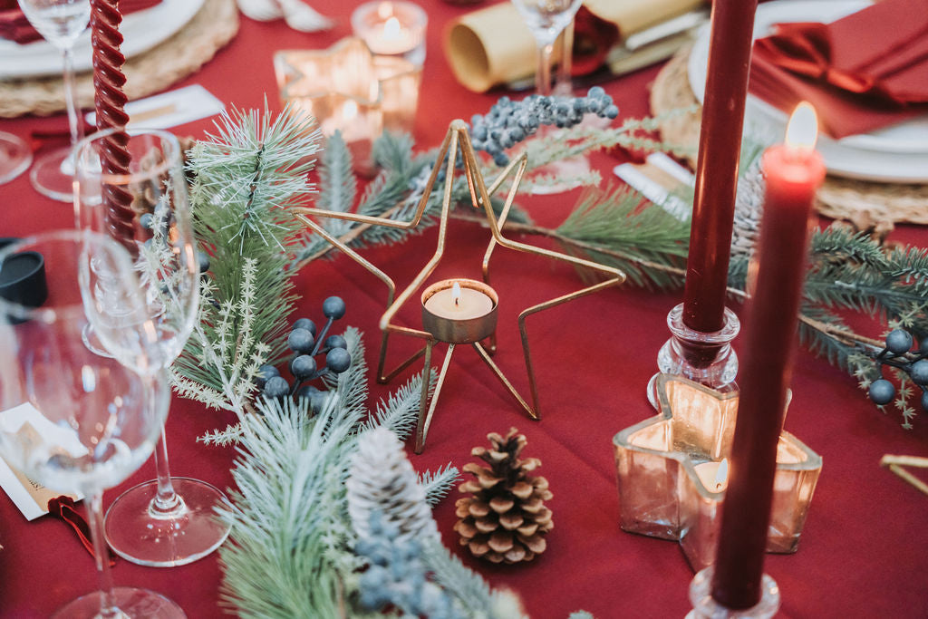 Decorative table setting with dark red candles, glasses, and festive elements on a dark red tablecloth, designed by Noble & Nordic.
