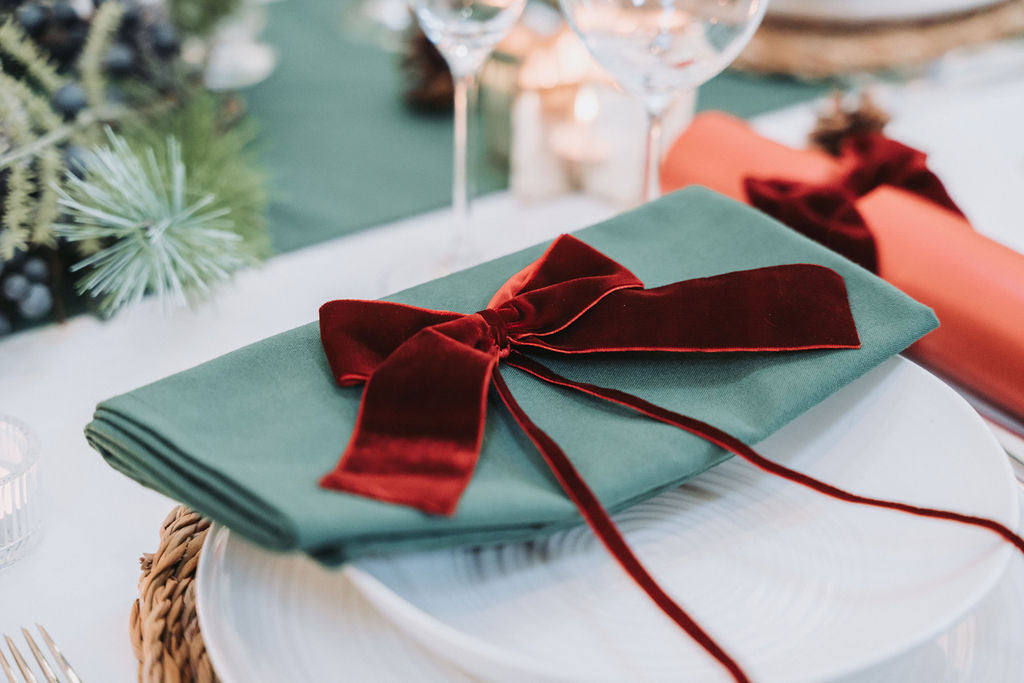 Pine forest green and red velvet Christmas table setting for six with crackers and warm candlelight by Noble & Nordic.