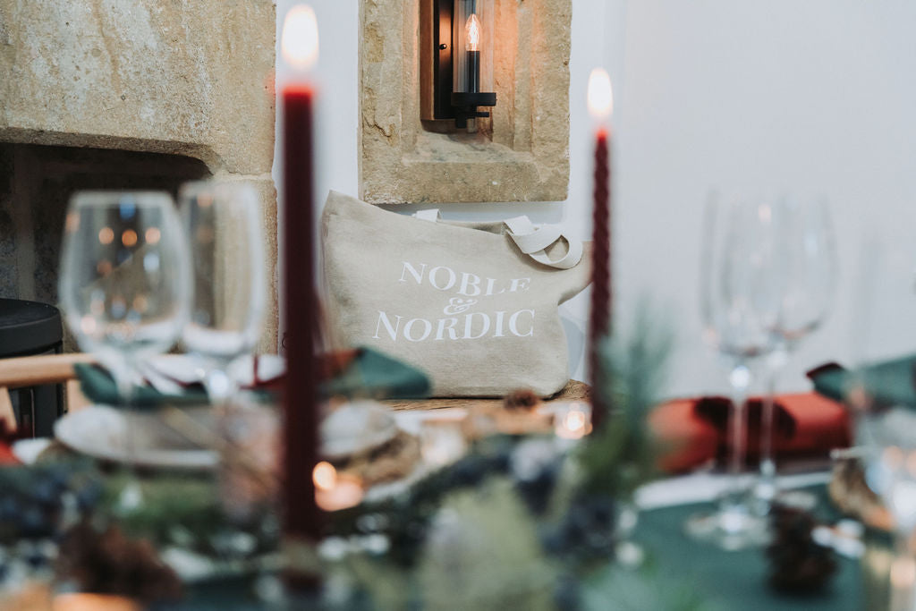 Noble & Nordic branded just bag by Christmas table styled in pine forest green table lines with burgundy velvet bows and candlelight.