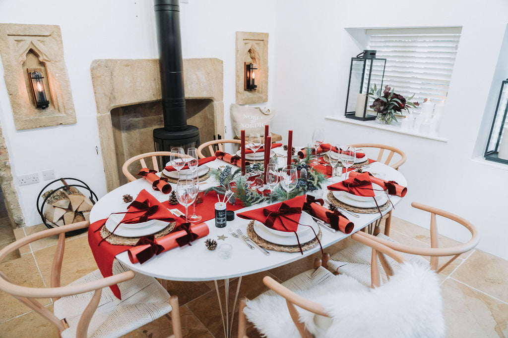 Elegant red Christmas table with burgundy velvet ribbons and glowing candlelight styled by Noble & Nordic.