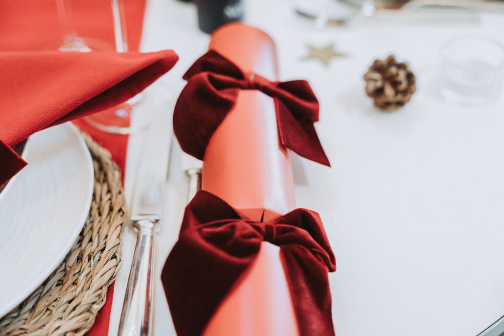 Modern red Advent table styled with candles, hand rolled red Christmas crackers, and burgundy velvet bows by Noble & Nordic.