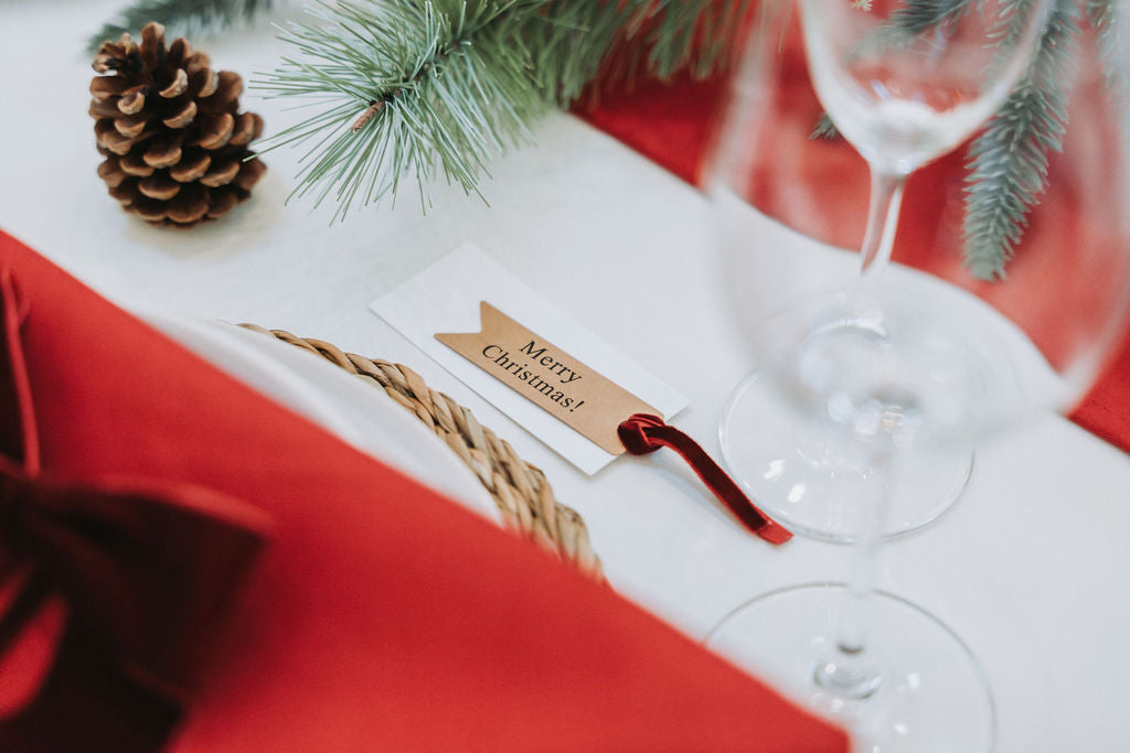 Close-up of name card, candlelight reflecting off red napkins and Christmas fir pine cone garland decorations in a Nordic Christmas setting by Noble & Nordic.