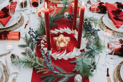 Red Advent tablescape featuring red candles, pine foliage Christmas garland, and gold star tea-light candleholders by Noble & Nordic.