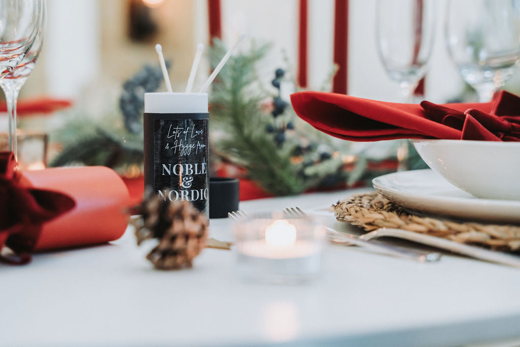 Detail of festive table styling with matchsticks, pinecones, burgundy velvet bows, and red taper candles by Noble & Nordic.