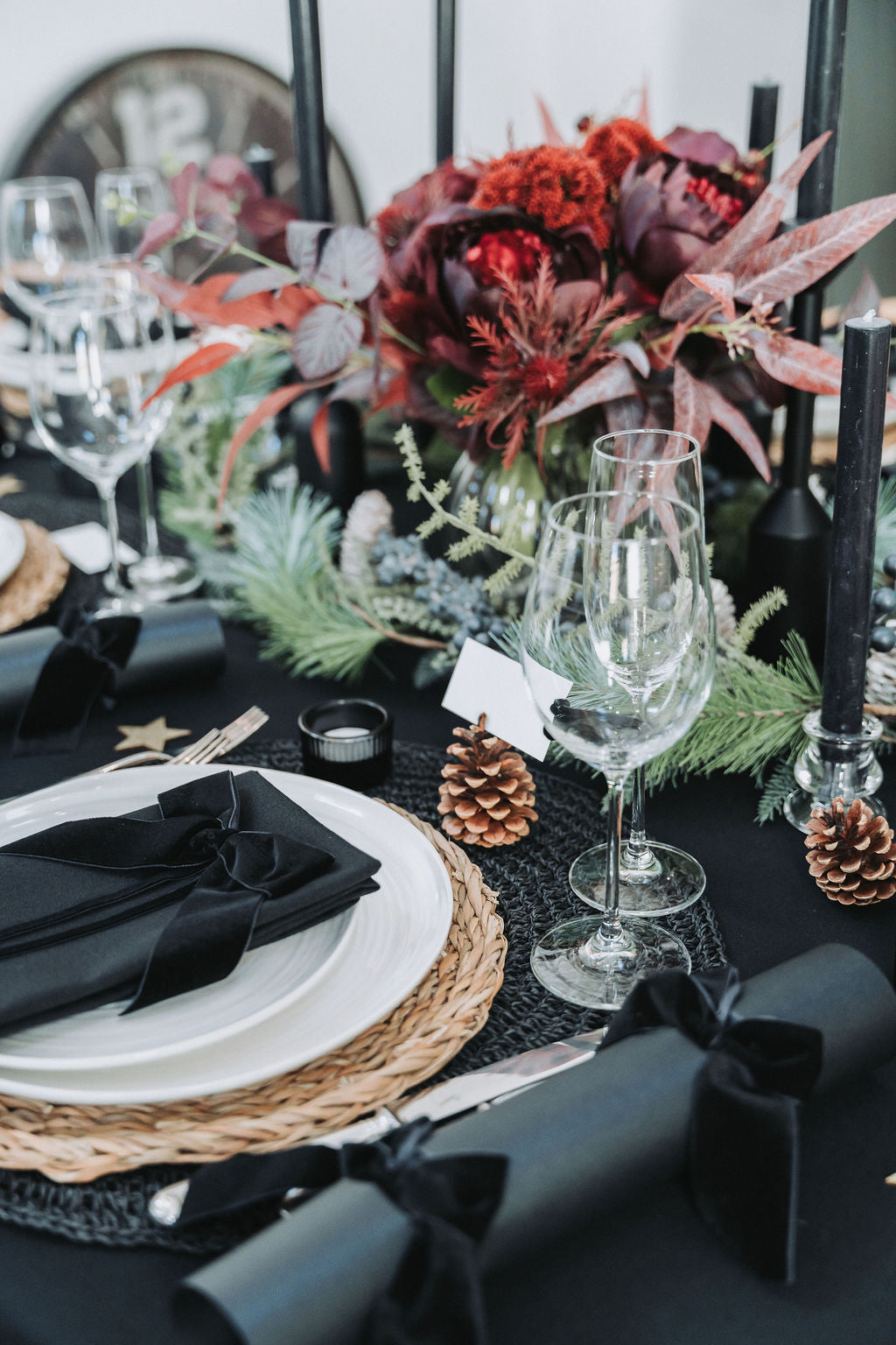 Black Pearl Christmas tablescape featuring black velvet bow crackers, pinecones, crystal glassware and deep red florals — refined Nordic festive styling by Noble & Nordic.