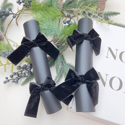 Black Christmas cracker with black velvet bows on a decorative background with Christmas fir pine cone garland by Noble & Nordic.