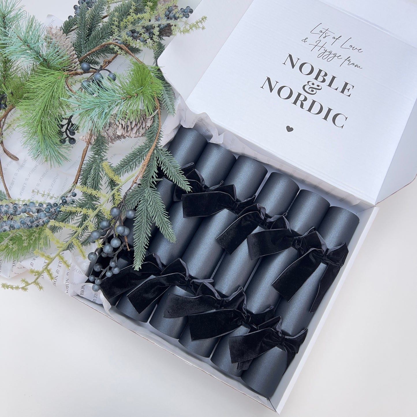 Box of black Christmas crackers with black velvet bows with 'Noble & Nordic' branding on a decorative gift box by Noble & Nordic.