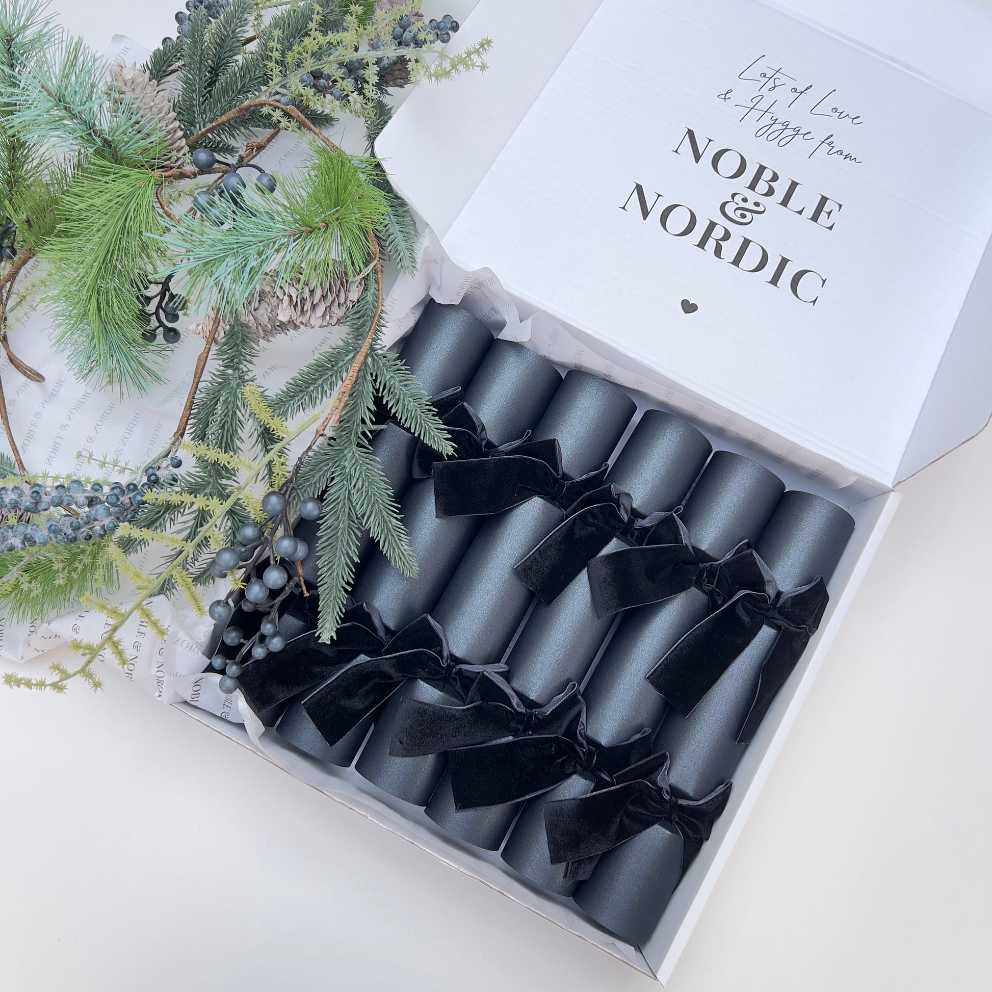 Box of black Christmas crackers with black velvet bows with 'Noble & Nordic' branding on a decorative gift box by Noble & Nordic.