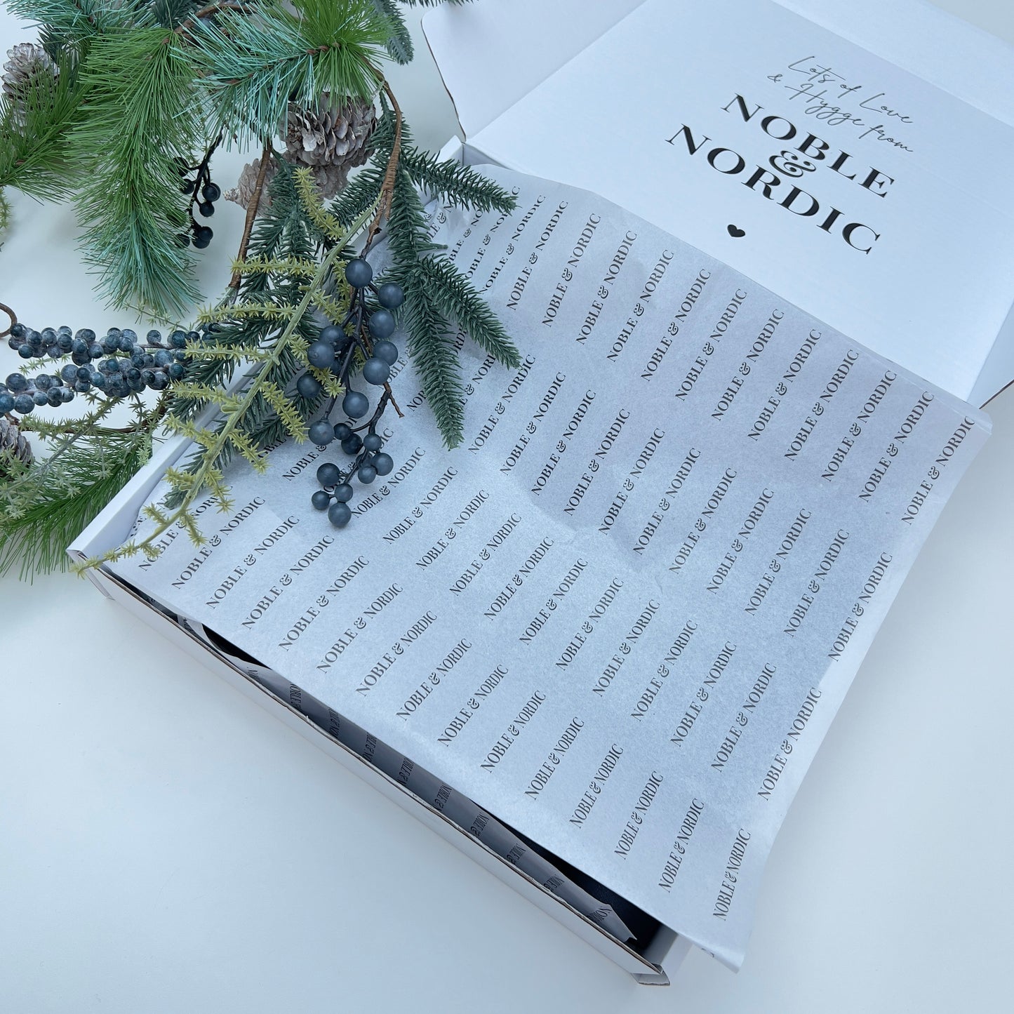 Open Christmas cracker packaging with 'Noble & Co.' branding, featuring decorative Christmas fir pine cone garland on a white background designed by Noble & Nordic.