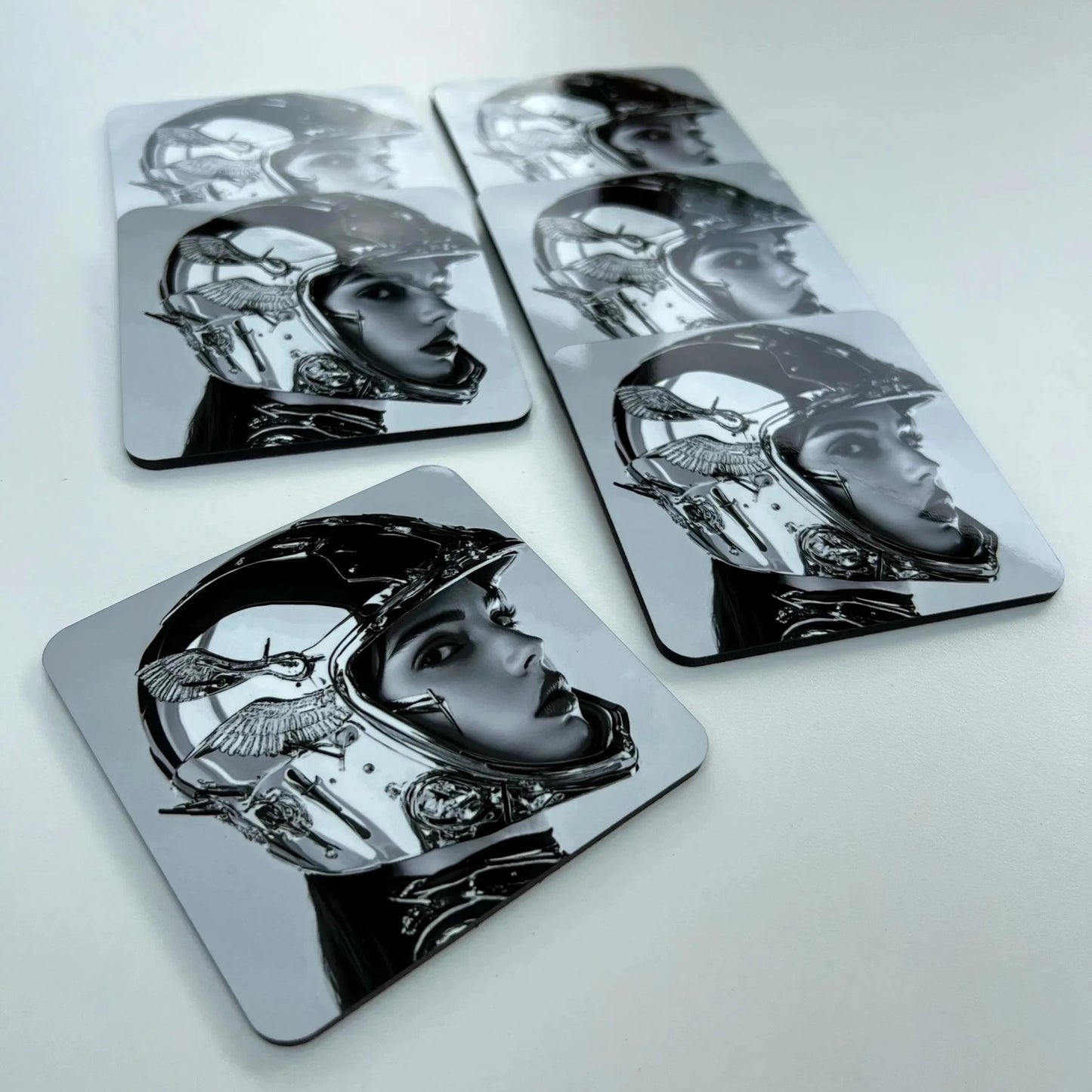 Set of four metallic coasters with black and white illustrations on a light gray background