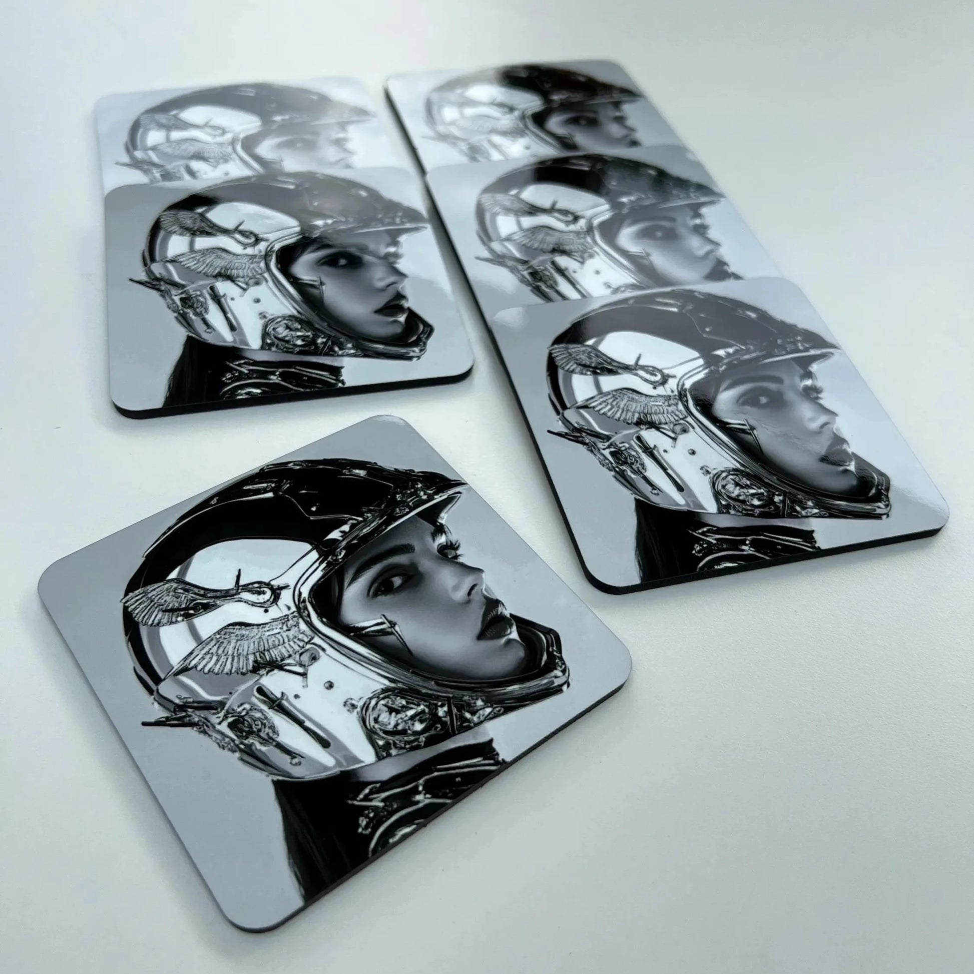 Set of four metallic coasters with black and white illustrations on a light gray background