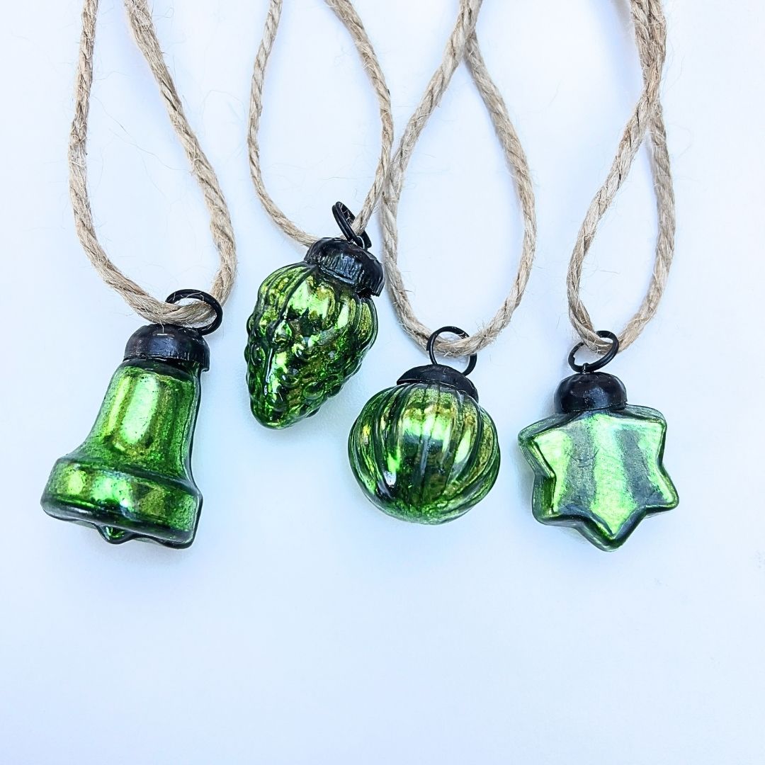 Four green glass Christmas baubles on strings against a white background