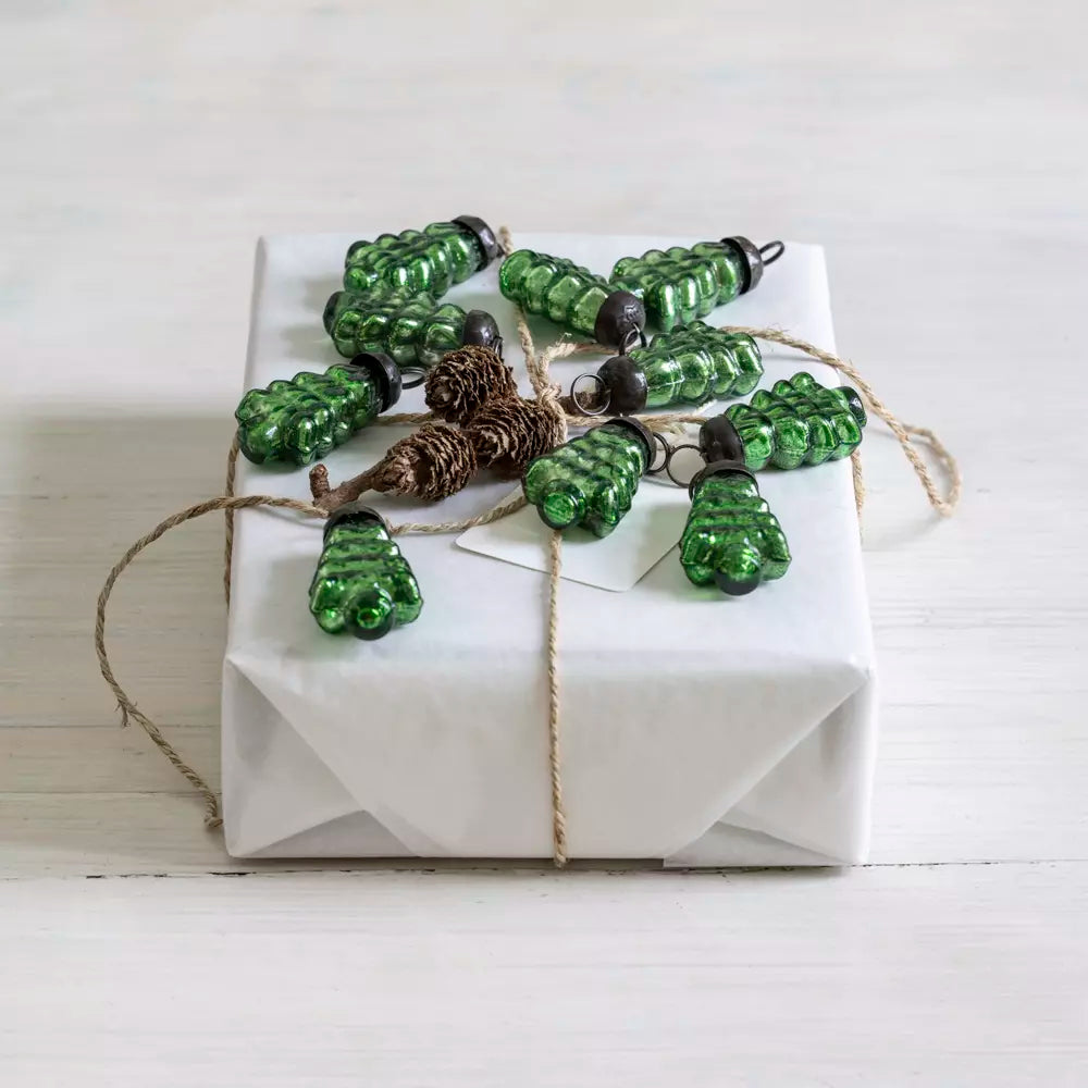 Set of small green glass Christmas tree baubles styled on a white wrapped gift with natural twine and pinecone — Noble & Nordic Nordic-inspired festive décor.