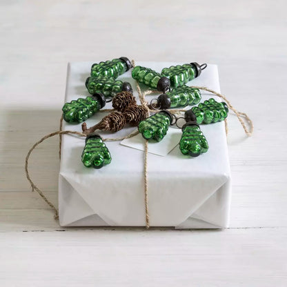 Set of small green glass Christmas tree baubles styled on a white wrapped gift with natural twine and pinecone — Noble & Nordic Nordic-inspired festive décor.