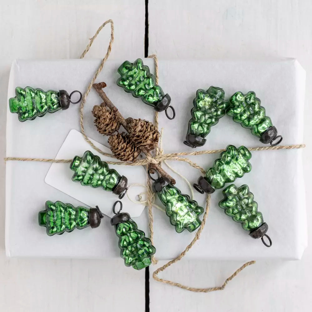 Green glass Christmas tree baubles styled on a white wrapped gift with natural twine and pinecone detail — elegant Nordic Christmas décor by Noble & Nordic.