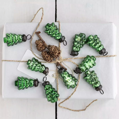 Green glass Christmas tree baubles styled on a white wrapped gift with natural twine and pinecone detail — elegant Nordic Christmas décor by Noble & Nordic.