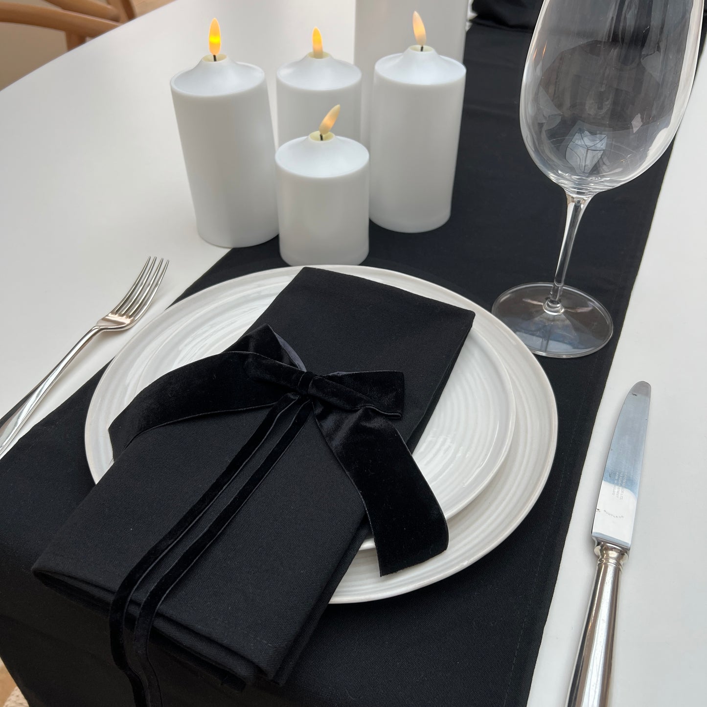Dining table setting with black napkin, white plates, silverware, and candles.