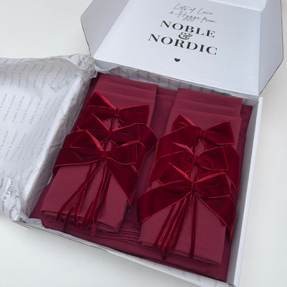 Red folded table linen with velvet bows in an open box labeled 'Noble & Nordic'.