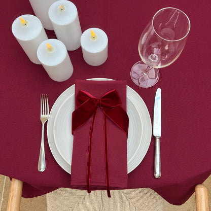 Dining table setting with burgundy napkin, white plates, silverware, and candles on a burgundy tablecloth.
