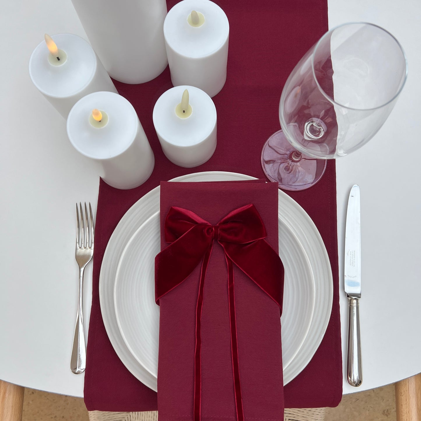 Dining table setting with burgundy napkin, white candles, and wine glass.