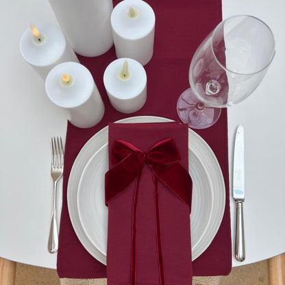 Dining table setting with burgundy napkin, white candles, and wine glass.