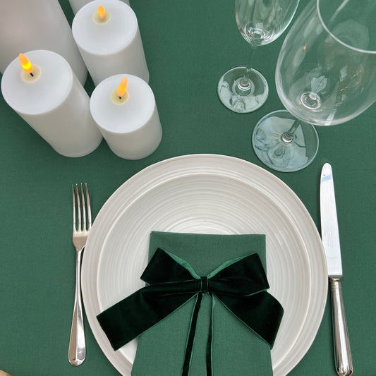 Dining table setting with white plates, silverware, green napkin, and candles on a green tablecloth.