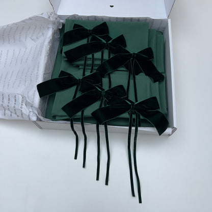 Dark Green Velvet bows on green table linen inside an open box with white interior.