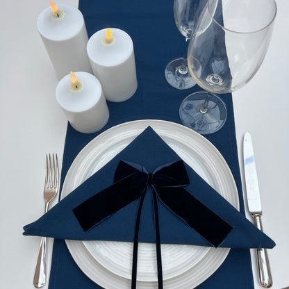 Navy blue napkin with a navy velvet bow on a white plate, surrounded by candles and glasses.