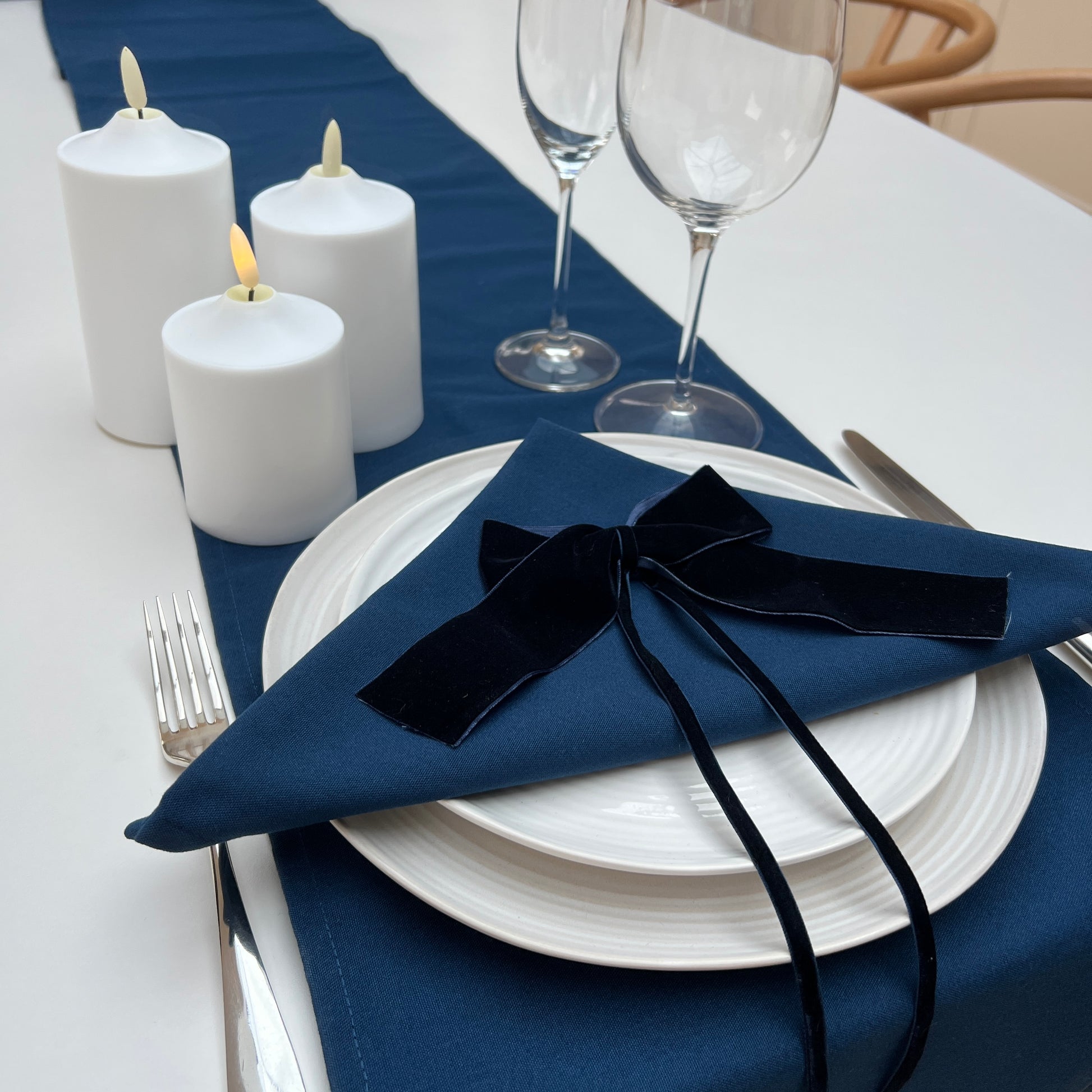 Elegant table setting with navy runner, white candles, and navy napkin with navy velvet ribbon.