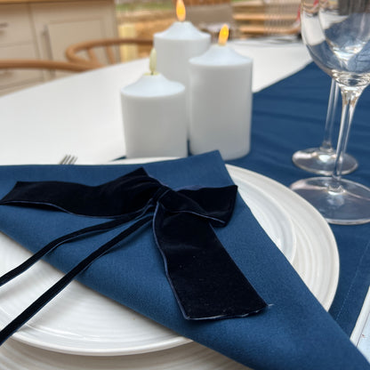Navy napkin with a navy velvet ribbon on a white plate, candles, and wine glasses in the background.