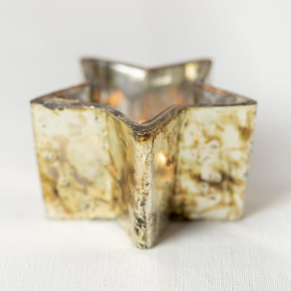 Close-up of copper tealight holder with perforated star design glowing warmly.